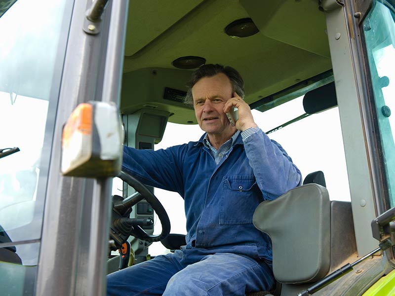 On-the-Go Decisions Rooted in Agronomic Expertise Farmer sitting in a tractor with the door open, talking on the phone in the field.